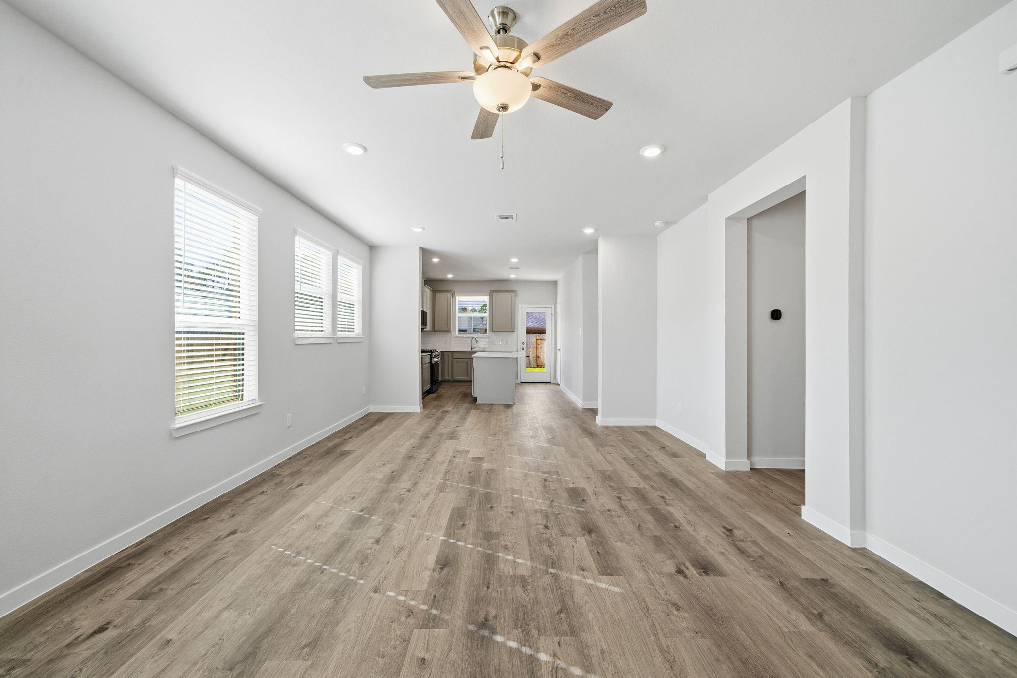 A large empty room with a ceiling fan and a wood floor.