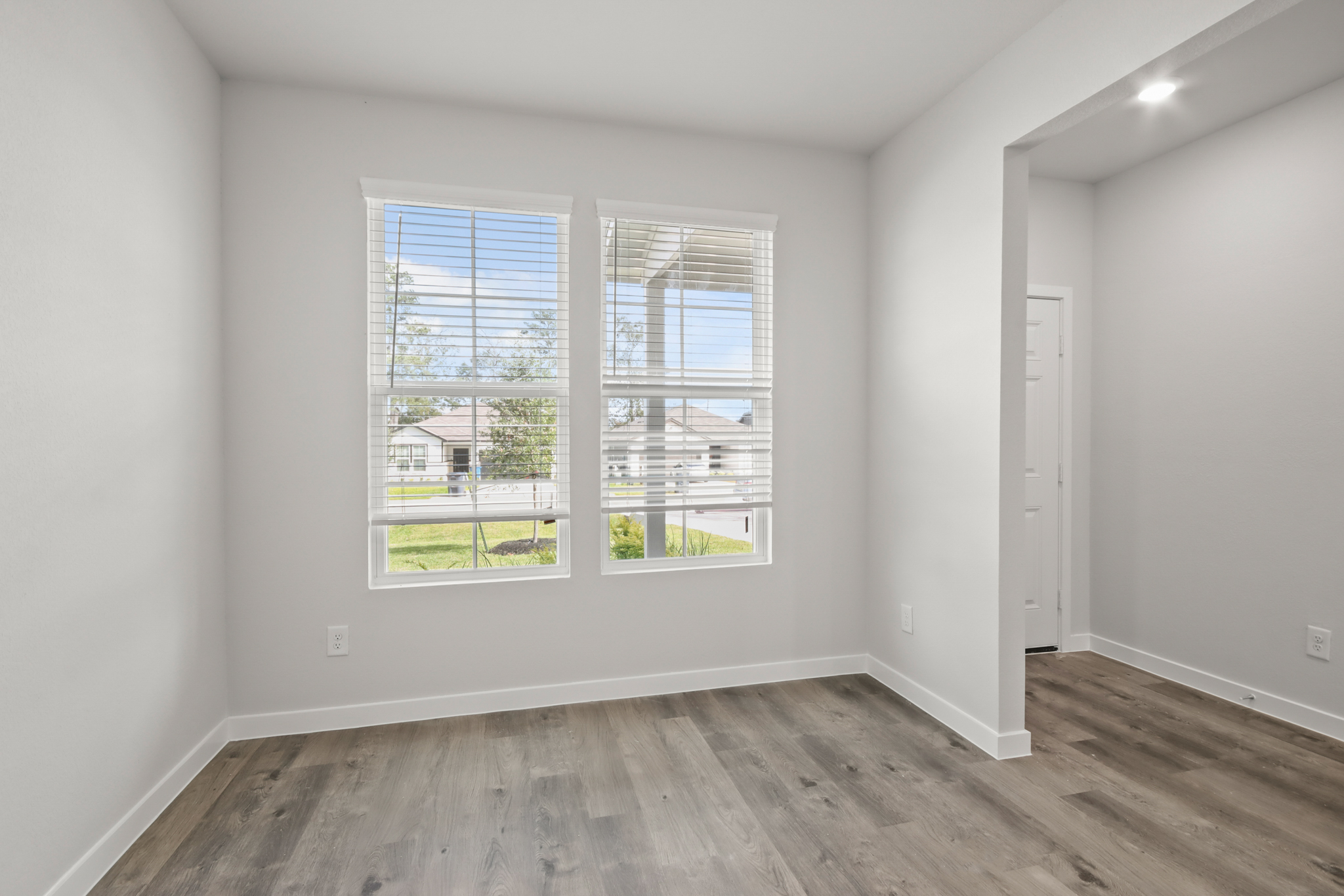 A room with a wood floor and a window with a view of a street and trees.