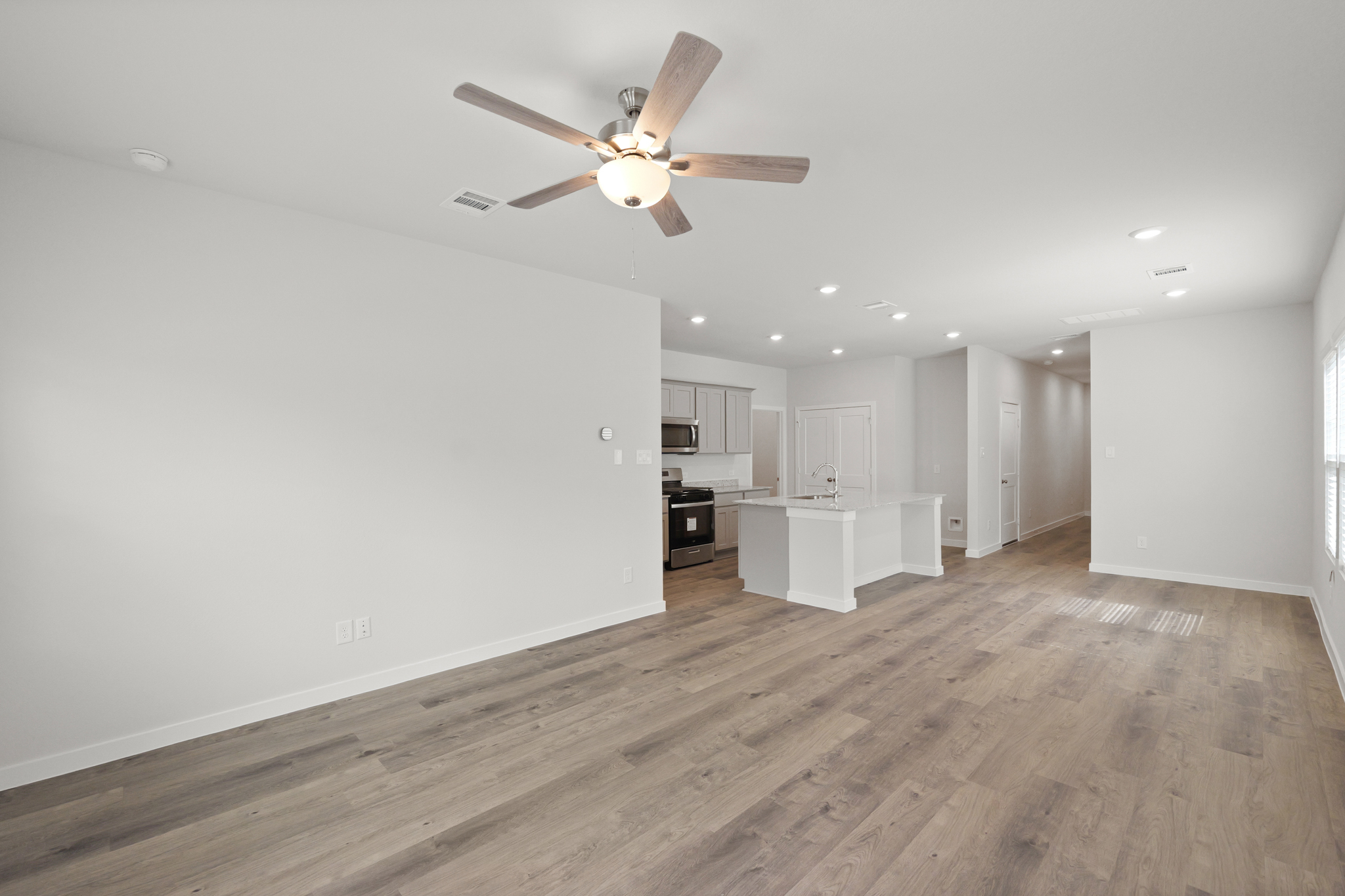 A large empty room with a ceiling fan and a wood floor.